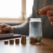 A person dropping a coin into a jar.
