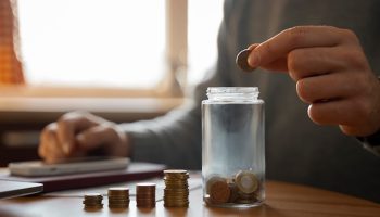 A person dropping a coin into a jar.