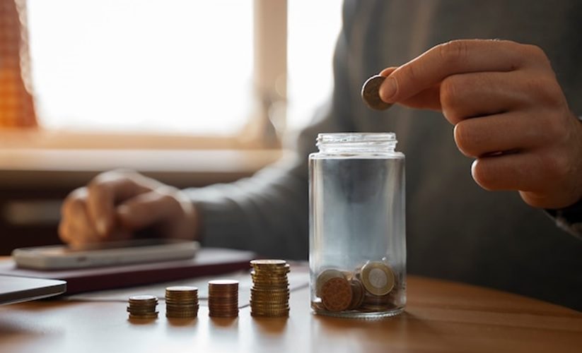 A person dropping a coin into a jar.